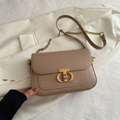 Taupe vierkante crossbodytas met gouden T-slot op een witte blazer achtergrond - Khaki