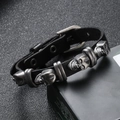 Close-up of punk black leather bracelet with three vintage silver skull metal charms - Black
