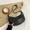 Bolso de hombro negro de media luna con herrajes dorados sobre fondo de traje beige - Negro