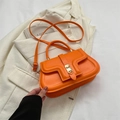 Leuchtend orangefarbene Satteltasche aus Leder mit Metallverschluss auf weißem Anzug - Orange