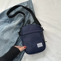 Navy blue nylon crossbody bag with Hello Weekend label on white bed and denim backdrop - Blue