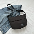 Minimalist black nylon crossbody bag with adjustable strap on denim jacket background - Black