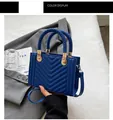 Detail of blue leather handbag with V-quilted pattern and woven handle on grey blazer - Blue