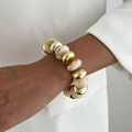 Detail eines Perlenarmbands mit goldfarbenen und weiß marmorierten Perlen am Handgelenk - Weiß