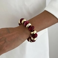 Detail eines Perlenarmbands mit goldenen Metallringen und roten Harzgliedern - Rot