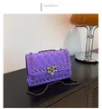 Detail of purple quilted crossbody bag with metal rivets and chain strap on wood surface - Purple