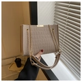 Detail of apricot crocodile pattern bag with gold hardware and woven strap in sunlight - Khaki