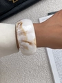 Detailopname van een brede armband van marmerhars met witte en bruine textuur om pols - Crèmewitte brede harsarmband met marmertextuur (0080)