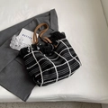 Checkered woven tote bag with black fringes and brown leather handles in flat lay view - Black