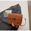 Brown crossbody bag with white stitching and dark toggle button closure in hand - Brown