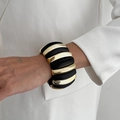 Detail eines klobigen schwarz-goldenen Armreifs getragen über einem weißen Blazer - Schwarz Gold Block Spleißstil (0155) / Schwarz