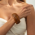 Detailopname van een brede marmeren barnsteenkleurige hars armband op een model - Geelbruin (Barnsteen)