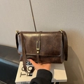 Detailed view of a retro brown PU leather shoulder bag with metallic buckle on a book - Brown