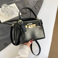 Glossy black crocodile pattern leather handbag with gold buckle in an aesthetic setting - Black