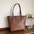 Vista dettagliata della borsa tote marrone intrecciata su uno scaffale con fiori - Marrone