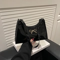 Detail of black patent leather underarm bag featuring a metallic gold bow on white decor - Black