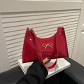 Close-up of glossy red patent leather shoulder bag with a gold bow metal buckle detail - Red