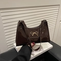 Detail of dark brown patent leather underarm bag featuring a golden metal bow buckle - Brown