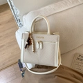 Detail of beige woven tote bag with white faux leather trim and beaded tassel charm - With Pendant / White