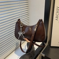 Chic dark brown patent leather crescent bag with silver metallic bow charm on white background - Brown