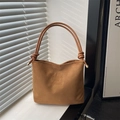 Braune Wildleder-Eimertasche mit Knotengriff und Gravur vor Fenster-Schatten-Hintergrund - Braun