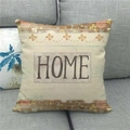 Detalle de funda de cojín de lino con texto HOME y flores sobre un sofá de tela gris - Home Grano de Madera Vintage