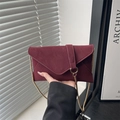 Elegant burgundy envelope bag with matte finish and gold chain strap held by model - Red