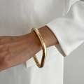 Close-up of irregular chunky gold wavy bangle worn on wrist with minimalist white clothing - Gold-0162