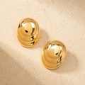 Close-up of geometric oval gold button earrings on a textured beige sand background - Gold
