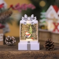 Close-up of glowing Christmas gift box snow globe with skier and sparkling glitter - White Snowman with Tree
