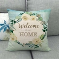 Detalle de funda de cojín de lino con guirnalda floral y texto Bienvenido a casa en sofá gris - Welcome to our HOME Guirnalda Azul