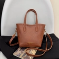 Bolso tipo cubo de cuero marrón con asas y correa ajustable sobre una silla - Marrón Oscuro