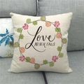 Detail eines Leinenkissenbezugs mit Love Never Fails Text und Kranz auf Sofa - Love NEVER FAILS Kranzstil(13)