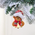 Detalle de oso de Navidad con gorro rojo y campana dorada en una rama de pino con nieve - Oso