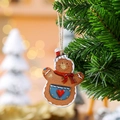 Hanging resin gingerbread man ornament with red hat on a green Christmas tree branch - Apron Style