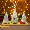 Detail von drei beflockten Mini-Weihnachtsbäumen mit warmen LED-Lichtern auf Holztablett - Schneebeflocktes Set