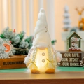 Close-up of glowing Christmas gnome plush with white faux fur and gold star embroidery - Gift Bag Style