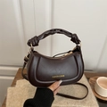 Dark brown half-moon handbag with knot handle and gold hardware on a wooden table - Coffee