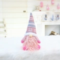 Vue détaillée d'un gnome de Noël rose avec bonnet en tricot flocon et barbe en peluche - Style Assis (Barbe Rose)