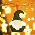 Gnomo di Natale in feltro fatto a mano appeso a un ramo con sfondo bokeh caldo - Verde