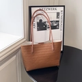 Braune geflochtene Leder-Tote-Bag mit Schultergurten auf modernem schwarzem Tisch - Braun