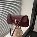 Burgundy litchi leather underarm bag with gold metal buckle shown in hand - Red