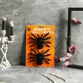 Close-up of realistic flocked black spiders on a decorative orange Happy Halloween card - 2 Small Spiders