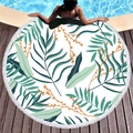 Round beach towel with tropical green leaf patterns and white fringe tassels on wood deck - Fresh Tropical Leaves Style