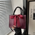 Deep red handbag with black woven handle and a large satin bow accent, crossbody style - Burgundy