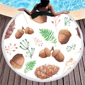 Round tropical leaf beach towel with white tassels displayed on a sunny poolside deck - Forest Plant Acorn Style (1)