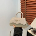 Elegant beige bow crossbody bag featuring rhinestone handle and stylish wavy bottom - Gold