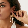 Detalle de pendientes dorados con estrella de mar y borlas en una modelo real - Dorado
