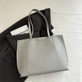 Minimalist light grey faux leather tote bag with metallic detail on office attire - Gray