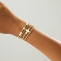 Detailweergave van een 4-delige gouden kralenarmbandset met wit kruisje en parels om de pols - Gouden Kruis 4-delige Set (06346)